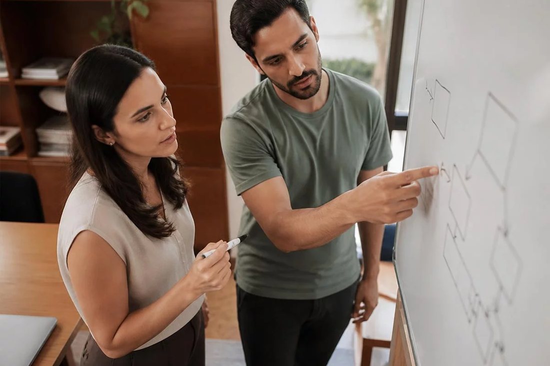 Facilitadora aponta para um mapa de argumento desenhado no quadro branco enquanto um participante acompanha